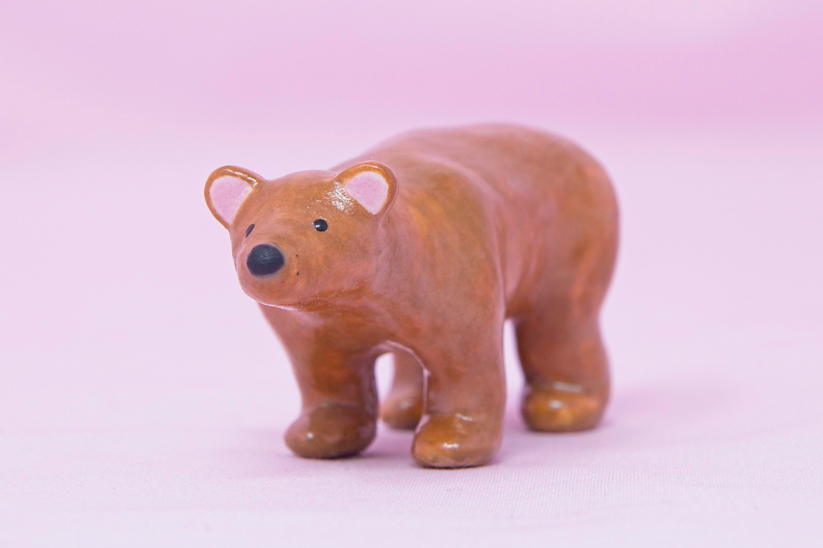 A handmade miniature ceramic brown bear against a pink background.