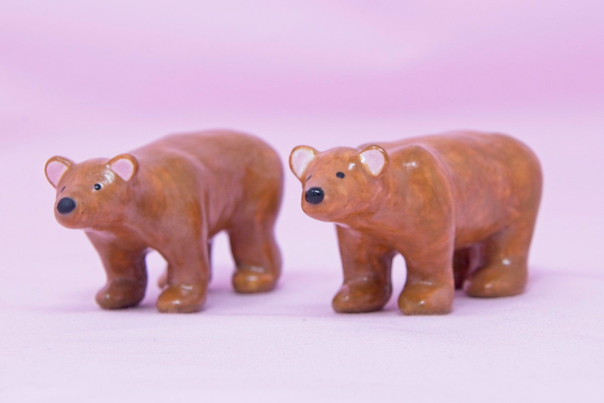 A pair of handmade miniature ceramic brown bears against a pink background.