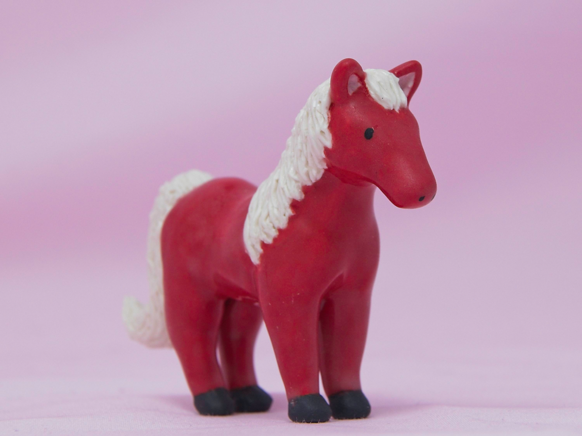A miniature red ceramic horse on a pink background.