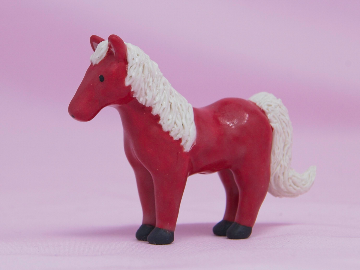 A miniature red ceramic horse on a pink background.