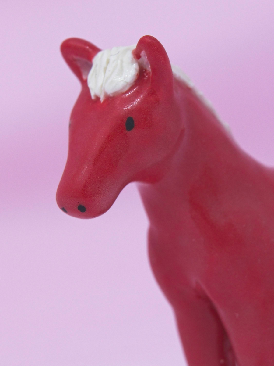 A miniature red ceramic horse on a pink background.