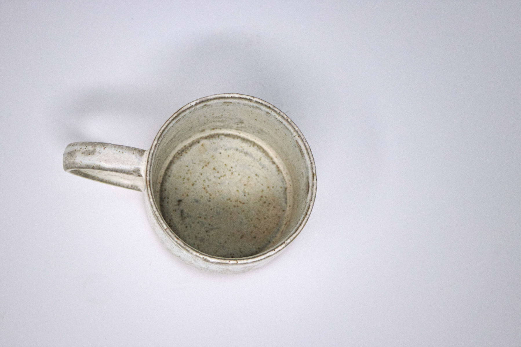 An overhead shot of a handmade white speckled mug, showing how the glaze breaks around the rim.