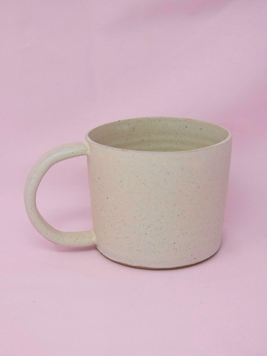 A handmade cream speckled mug against a pink background.