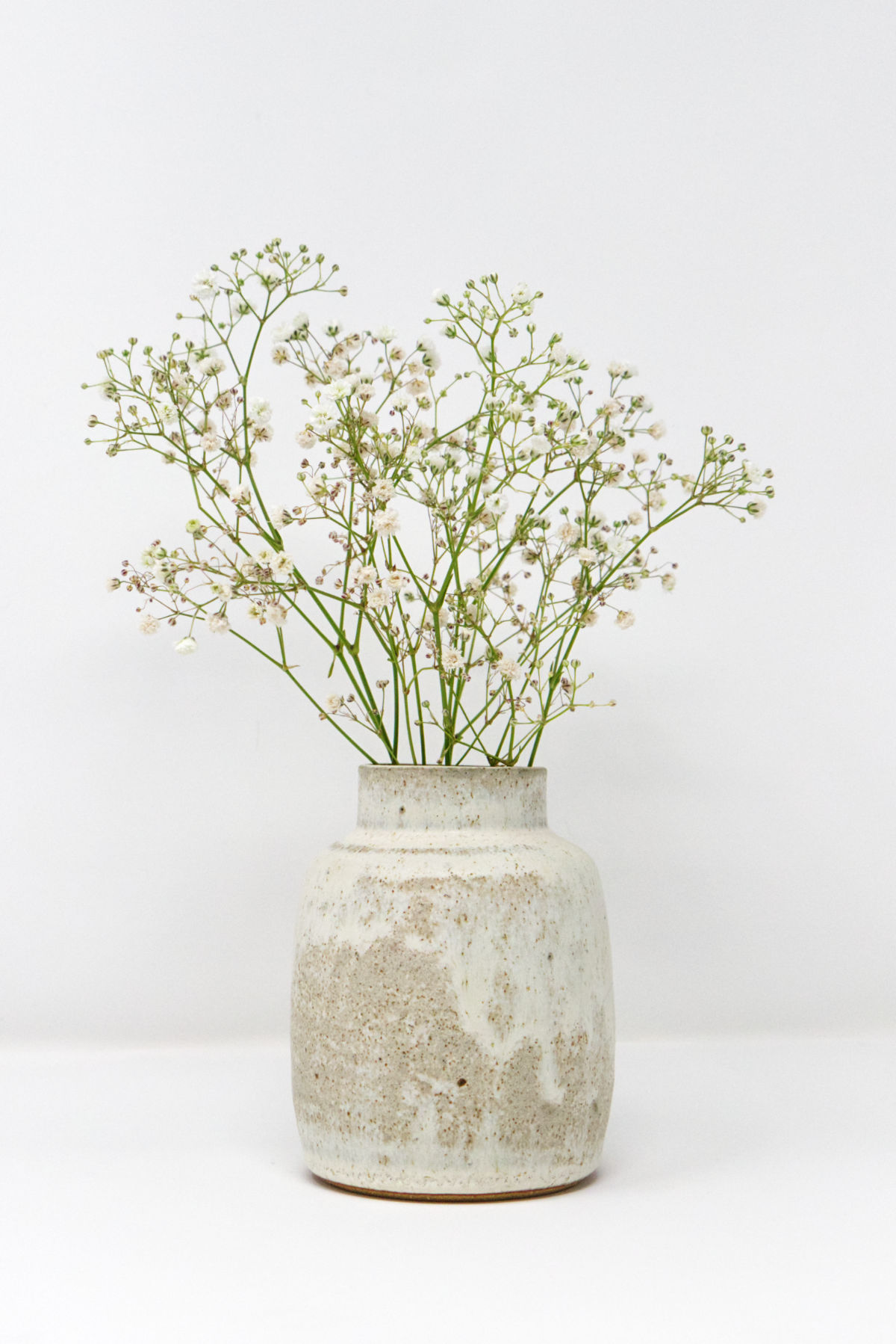 A handmade white speckled vase holding a bouquet of gypsophila.